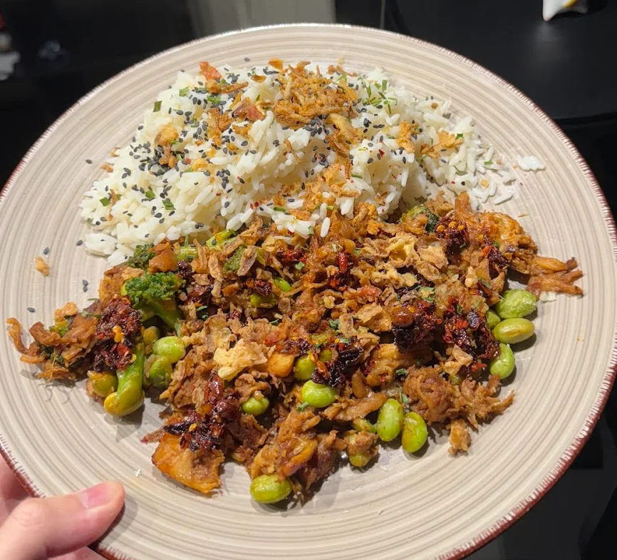 A plate of chicken, broccoli, and edamame with rice, chilli oil, and fried onions.
