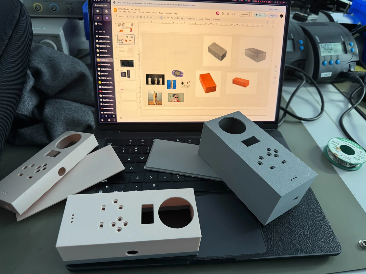 Several grey Brickphone enclosure parts laid out beside a laptop, with cutouts for the speaker, display, and controls.