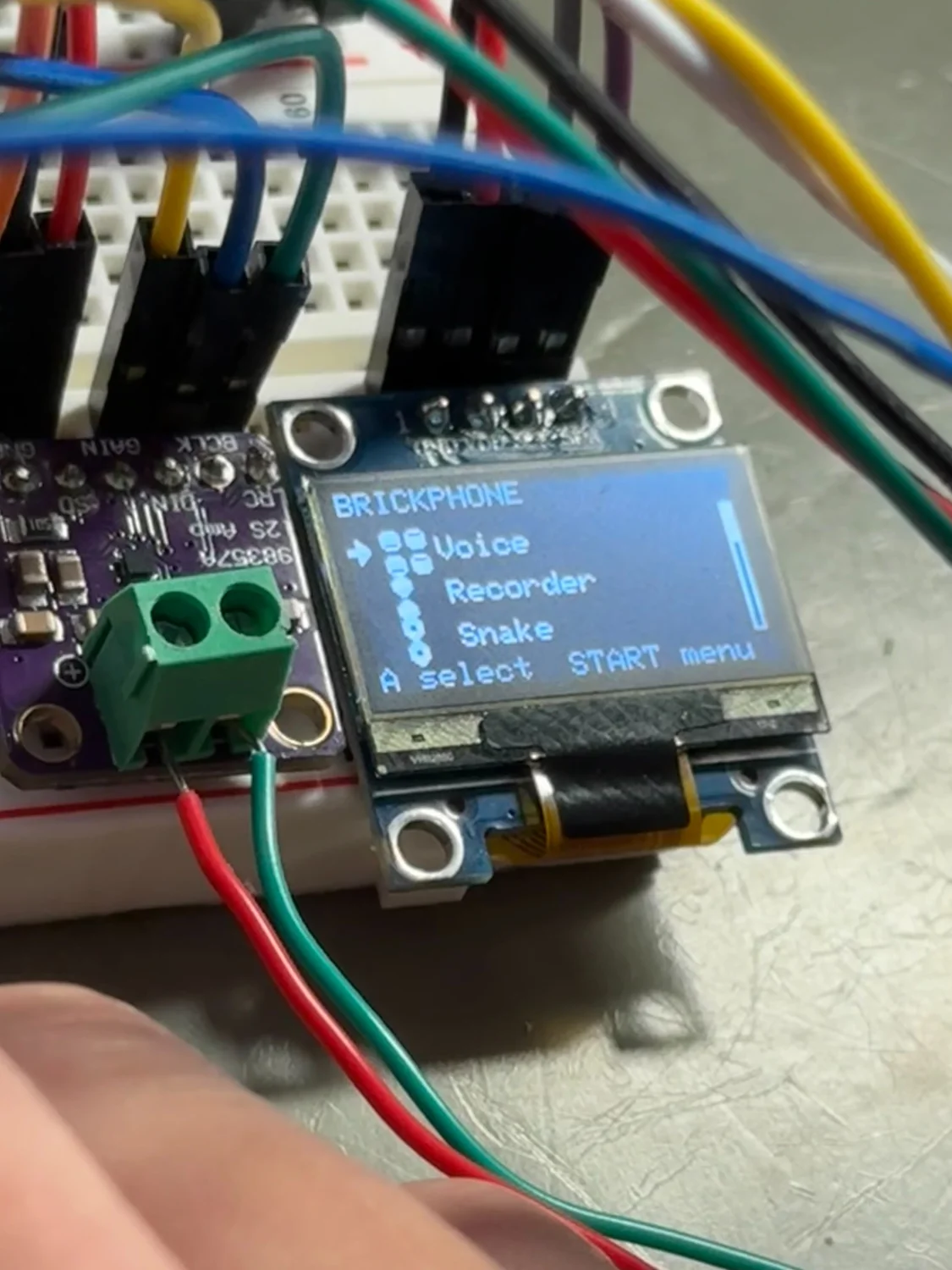 A powered OLED displaying the Brickphone menu, including Voice, Recorder, and Snake, beside the audio amplifier.